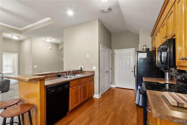 kitchen featuring a breakfast bar area, a peninsula, a sink, black appliances, and brown cabinets