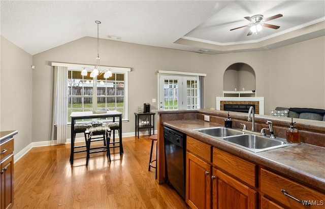 kitchen with a tiled fireplace, brown cabinetry, a sink, dishwasher, and light wood-type flooring