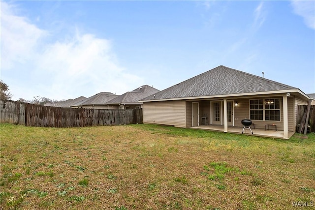 rear view of property featuring a yard, fence, roof with shingles, and a patio area