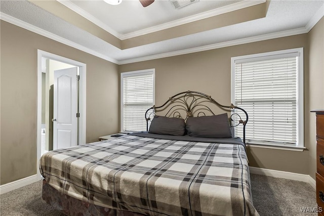 carpeted bedroom featuring a tray ceiling, baseboards, visible vents, and crown molding