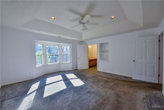 unfurnished bedroom with dark colored carpet, ceiling fan, ensuite bath, and a tray ceiling