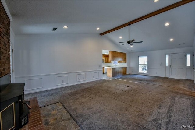 unfurnished living room with a fireplace, vaulted ceiling with beams, ceiling fan, and carpet flooring