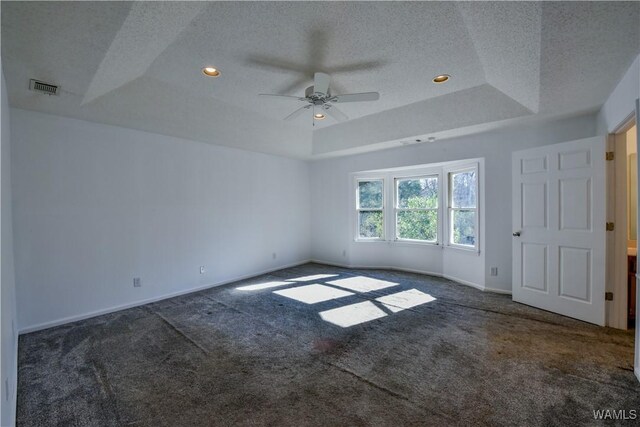 unfurnished room featuring a tray ceiling, ceiling fan, dark carpet, and a textured ceiling