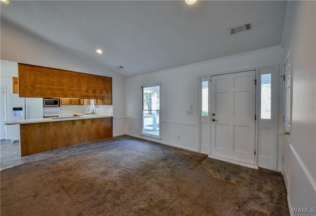 interior space with stainless steel microwave, white refrigerator with ice dispenser, kitchen peninsula, lofted ceiling, and dark carpet