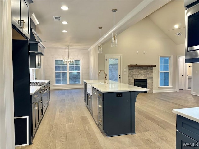 kitchen featuring a kitchen island with sink, high vaulted ceiling, hanging light fixtures, a fireplace, and light hardwood / wood-style floors