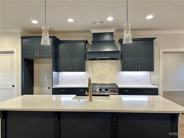 kitchen with pendant lighting, high end range, premium range hood, and a kitchen island with sink