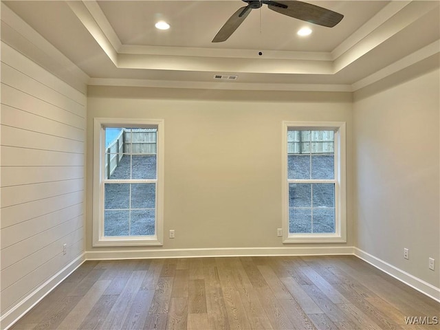 spare room with a raised ceiling, ceiling fan, a healthy amount of sunlight, and wood-type flooring