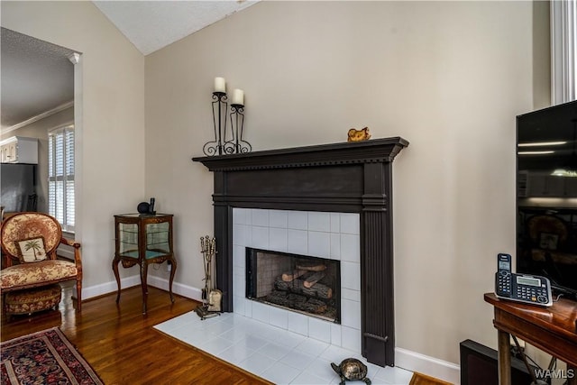 living room featuring lofted ceiling, wood finished floors, baseboards, and a tile fireplace