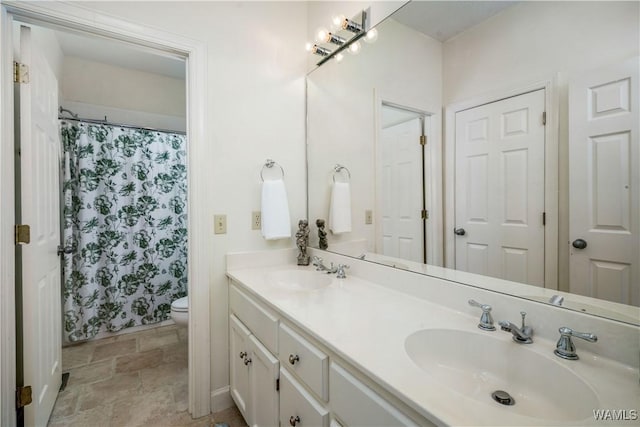 full bathroom with double vanity, stone finish floor, toilet, and a sink