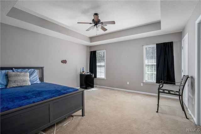 bedroom featuring a textured ceiling, a raised ceiling, baseboards, and light carpet