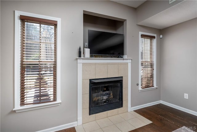 unfurnished living room with plenty of natural light, a tile fireplace, baseboards, and wood finished floors