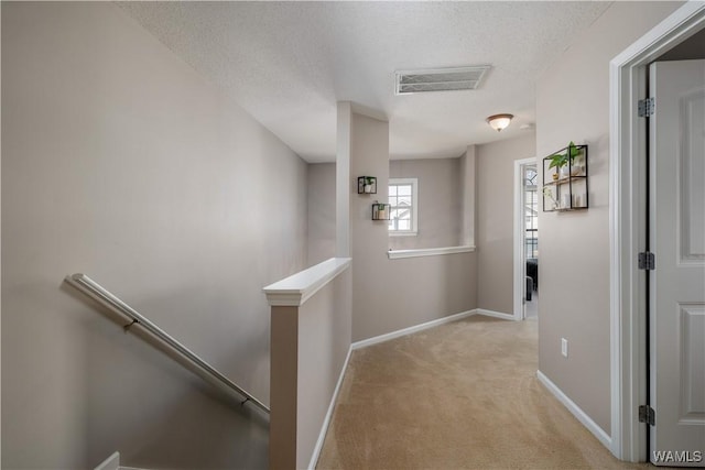 corridor with visible vents, baseboards, an upstairs landing, carpet flooring, and a textured ceiling