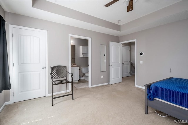 bedroom with a tray ceiling, baseboards, light colored carpet, and ensuite bathroom