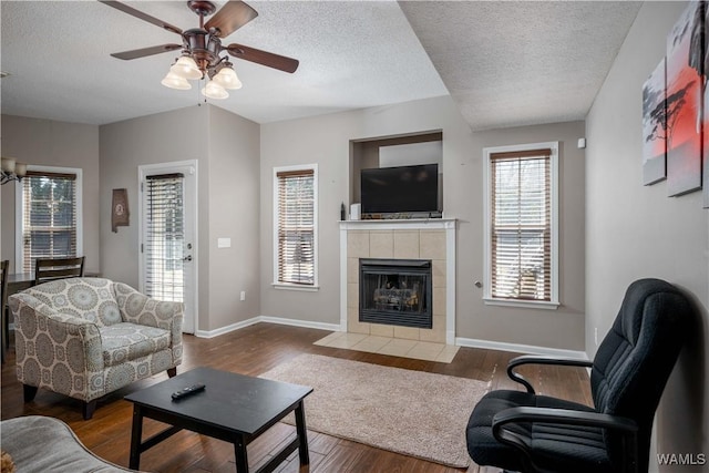 living area featuring a tiled fireplace, a textured ceiling, baseboards, and wood finished floors