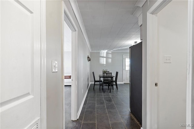corridor featuring dark tile patterned floors, ornamental molding, and baseboards