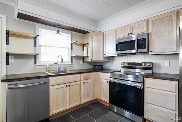kitchen featuring open shelves, light brown cabinetry, dark countertops, a sink, and appliances with stainless steel finishes