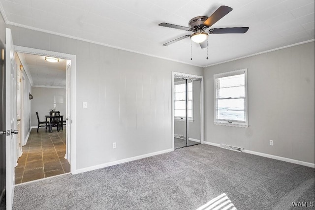 unfurnished bedroom featuring dark carpet, ornamental molding, a closet, and ceiling fan