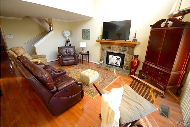 living room with a stone fireplace, crown molding, and hardwood / wood-style flooring