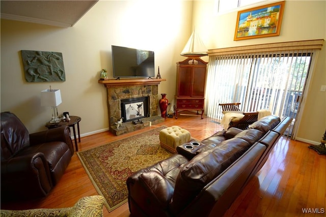 living room featuring a stone fireplace, wood-type flooring, and crown molding