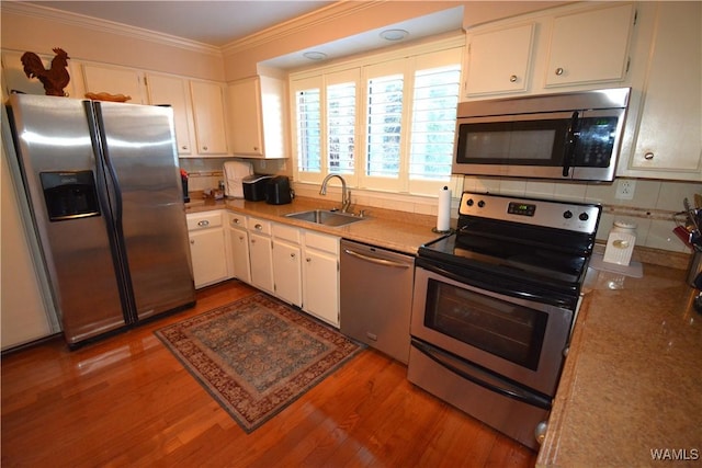 kitchen featuring appliances with stainless steel finishes, ornamental molding, sink, light hardwood / wood-style flooring, and white cabinetry