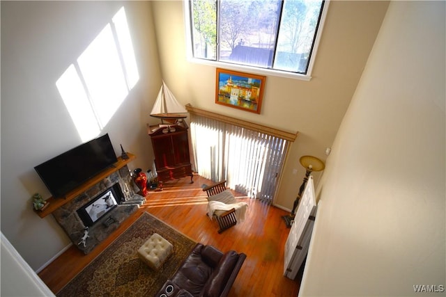 living room with a stone fireplace, a high ceiling, and hardwood / wood-style flooring