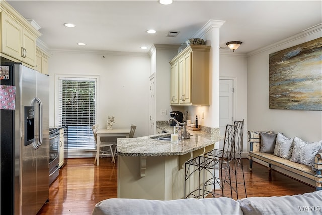 kitchen featuring a kitchen breakfast bar, dark wood-type flooring, cream cabinets, and stainless steel appliances