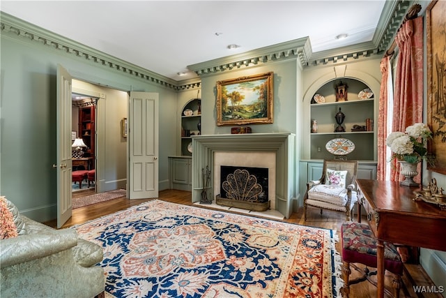 sitting room with built in shelves, crown molding, and wood-type flooring