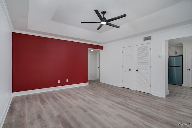 unfurnished bedroom with baseboards, visible vents, a raised ceiling, wood finished floors, and freestanding refrigerator