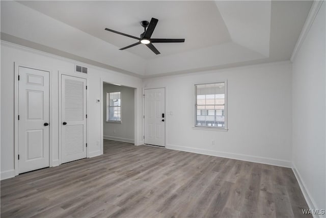 interior space featuring baseboards, a tray ceiling, a wealth of natural light, and wood finished floors