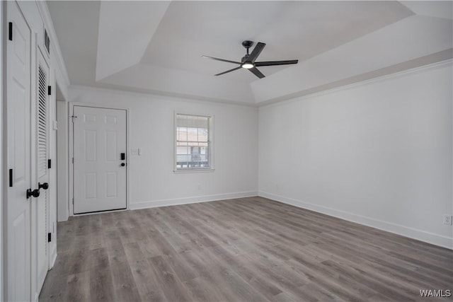 spare room featuring ceiling fan, wood finished floors, baseboards, ornamental molding, and a tray ceiling