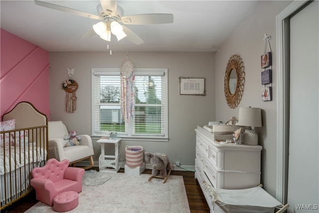 bedroom featuring ceiling fan, dark hardwood / wood-style flooring, and a crib