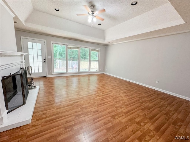 unfurnished living room with light wood-type flooring, a tray ceiling, a brick fireplace, and ceiling fan