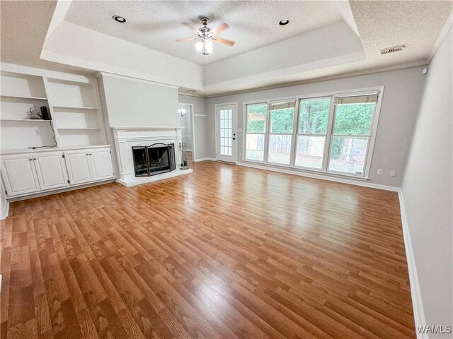 unfurnished living room with a raised ceiling, light hardwood / wood-style flooring, a textured ceiling, and built in features