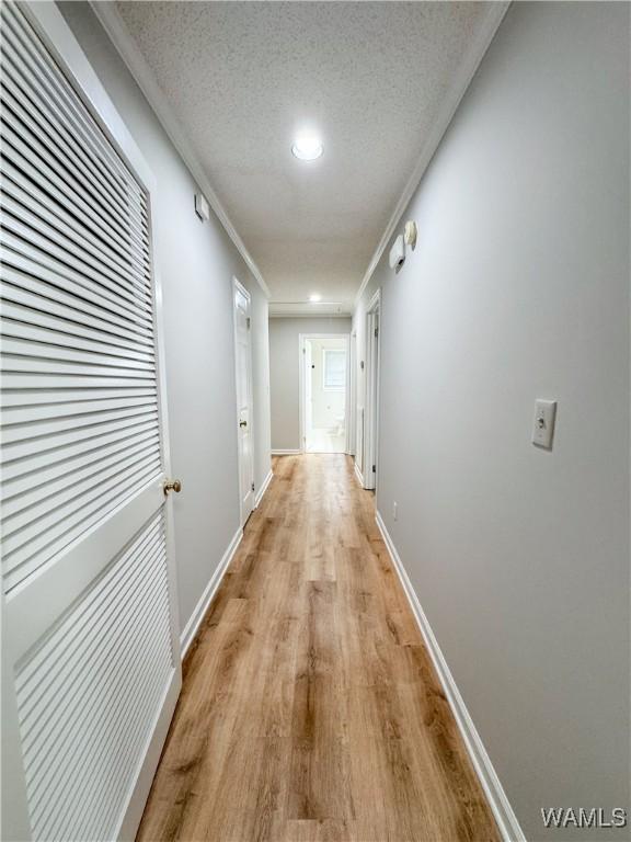 hall with a textured ceiling, light hardwood / wood-style floors, and ornamental molding