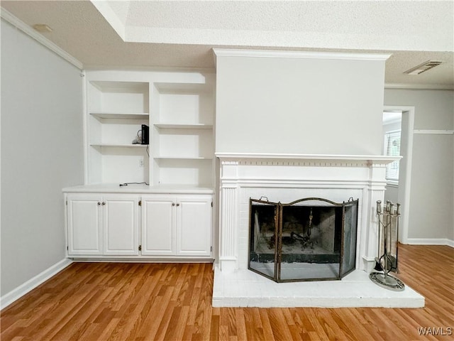 unfurnished living room featuring a textured ceiling, light hardwood / wood-style flooring, a brick fireplace, and ornamental molding