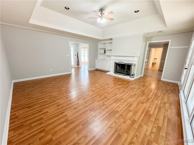 unfurnished living room featuring ceiling fan, light hardwood / wood-style floors, and a raised ceiling