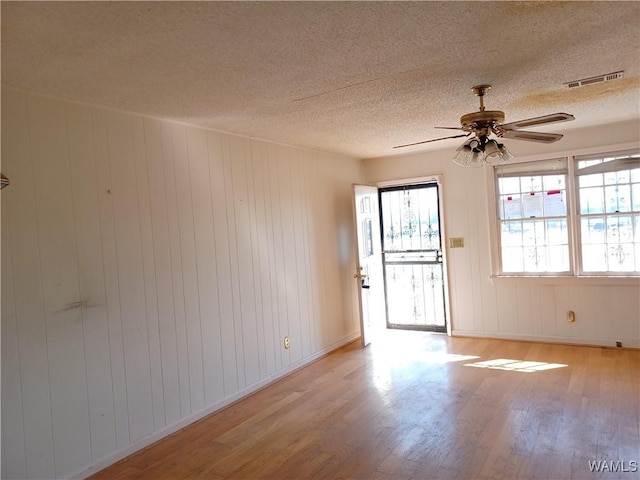 empty room with ceiling fan, a textured ceiling, visible vents, and wood finished floors