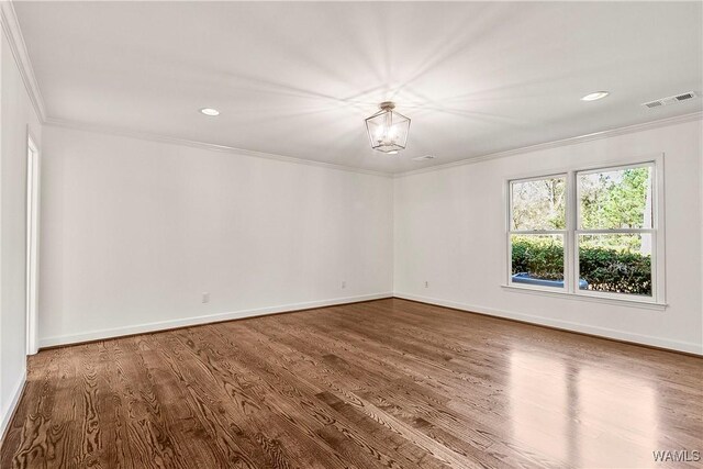 spare room featuring wood-type flooring, ornamental molding, and a notable chandelier