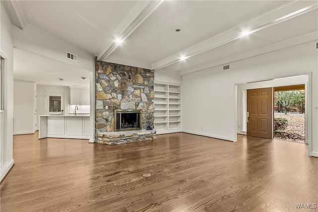 unfurnished living room featuring a fireplace, light hardwood / wood-style floors, sink, and beam ceiling