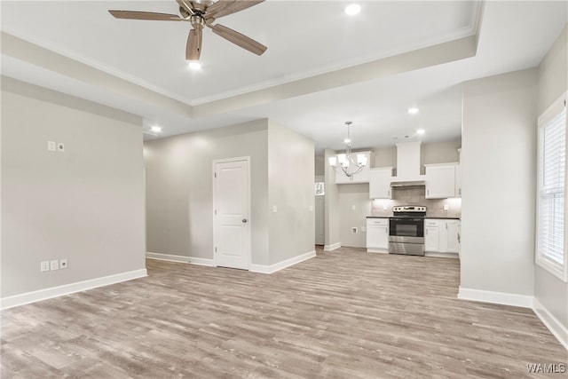 unfurnished living room with ceiling fan with notable chandelier, light wood-type flooring, ornamental molding, and a tray ceiling