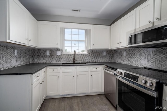 kitchen featuring visible vents, appliances with stainless steel finishes, wood finished floors, a sink, and dark countertops