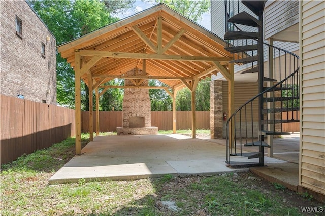 view of patio with a carport, a fenced backyard, a brick fireplace, and stairway