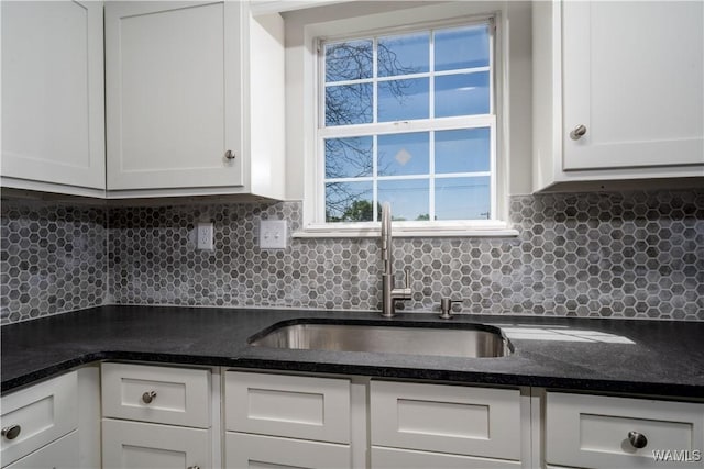 kitchen featuring tasteful backsplash, a sink, white cabinetry, and dark stone countertops
