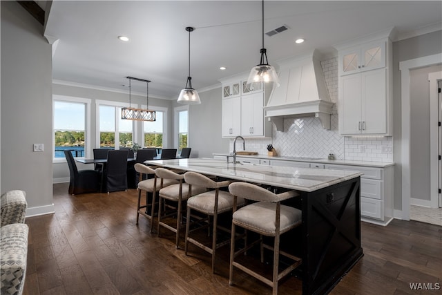 kitchen with white cabinets, premium range hood, dark hardwood / wood-style floors, a center island with sink, and a breakfast bar