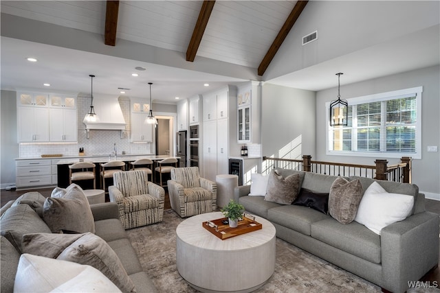 living room featuring sink, high vaulted ceiling, a notable chandelier, and beam ceiling