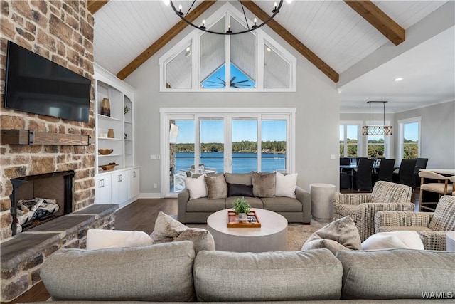 living room with a stone fireplace, a chandelier, beamed ceiling, and a water view