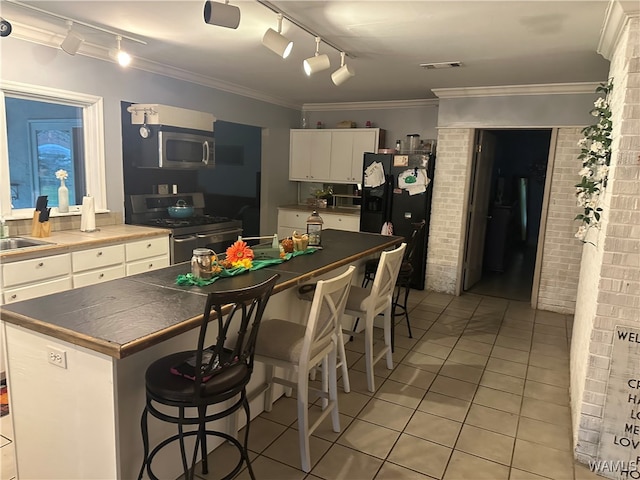 kitchen featuring white cabinetry, stainless steel appliances, brick wall, a kitchen island, and ornamental molding