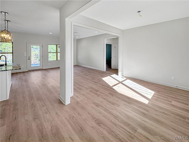 unfurnished living room featuring an inviting chandelier, sink, and light hardwood / wood-style floors