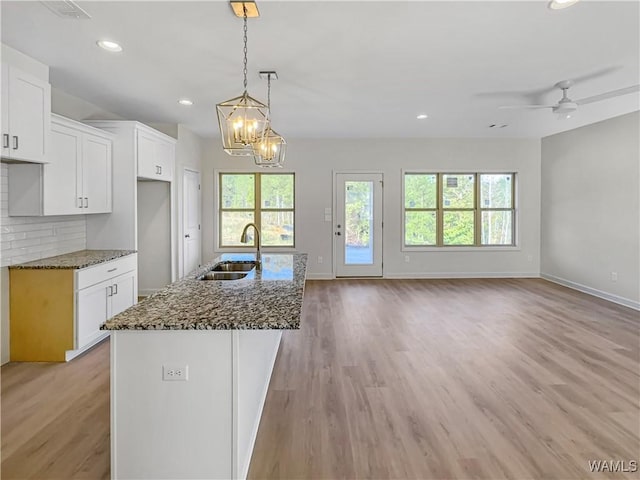 kitchen featuring sink, dark stone countertops, hanging light fixtures, an island with sink, and white cabinets