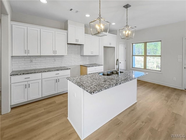 kitchen with stone countertops, pendant lighting, white cabinetry, sink, and a kitchen island with sink